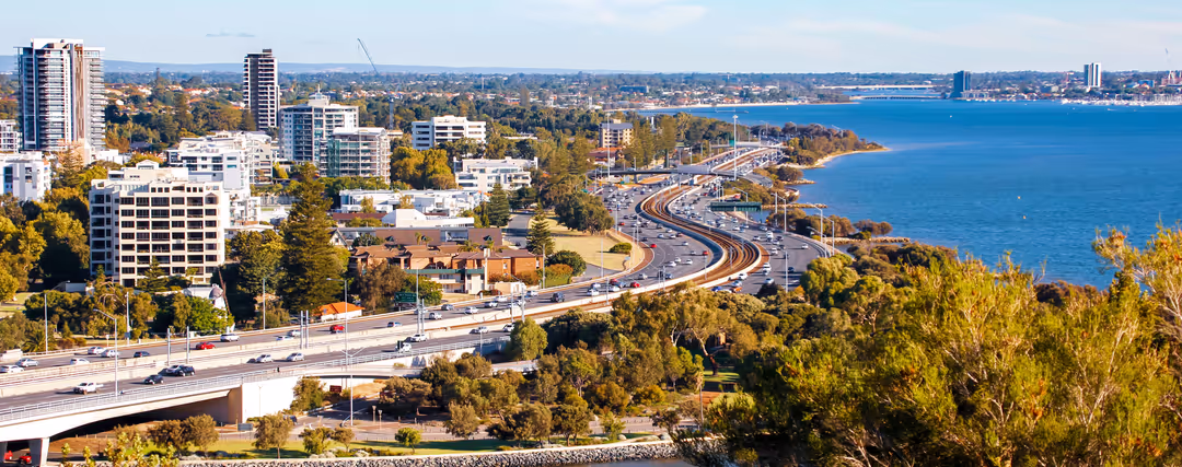 Perth skyline with its modern skyscrapers facing the River Swan under a deep blue sky.
